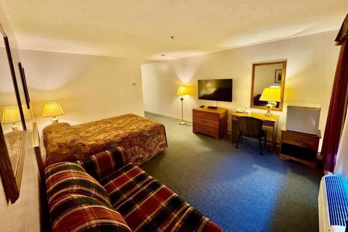 A hotel room with a bed, a desk, a chair, a television, and a lamp.