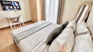 Quarto de hotel com cama, escrivaninha, cadeira e televisão exibindo um filme.