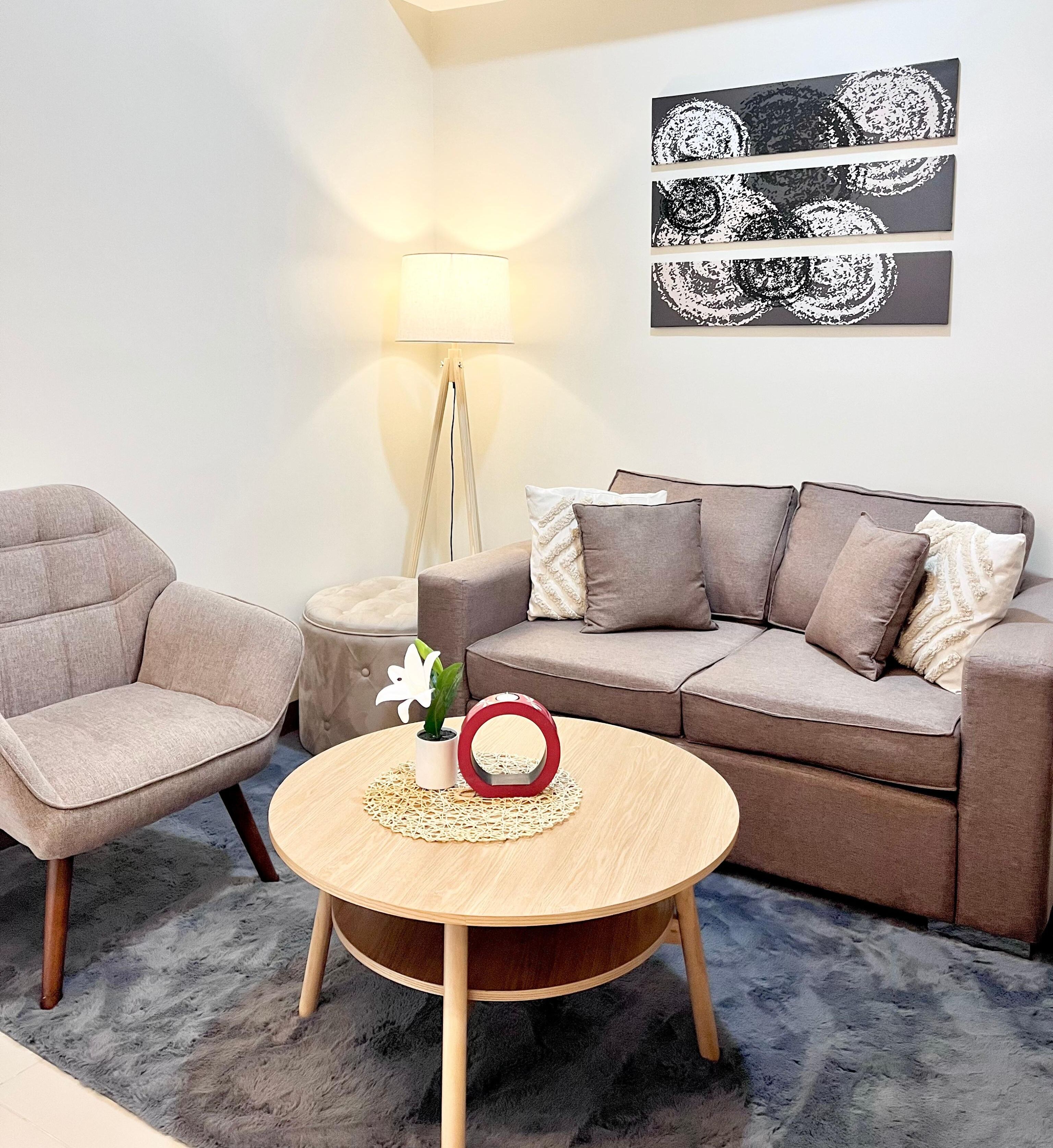 Un salon comprenant un canapé, un fauteuil, une table basse ronde, un lampadaire et des œuvres d’art murales.