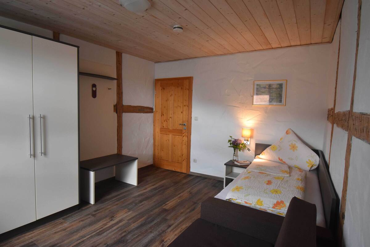 Une petite pièce comprenant un lit, une table de chevet avec une lampe, une porte en bois et une armoire.
