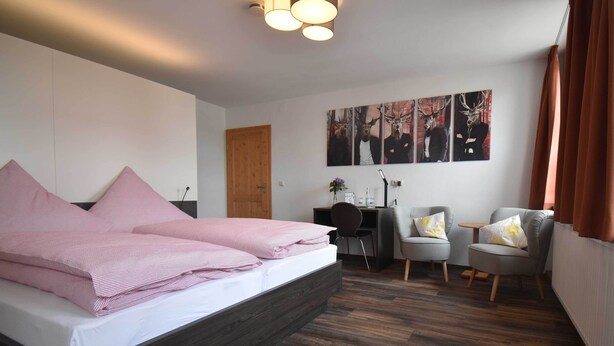 Een slaapkamer met een groot bed, een bureau, twee stoelen en een houten vloer.