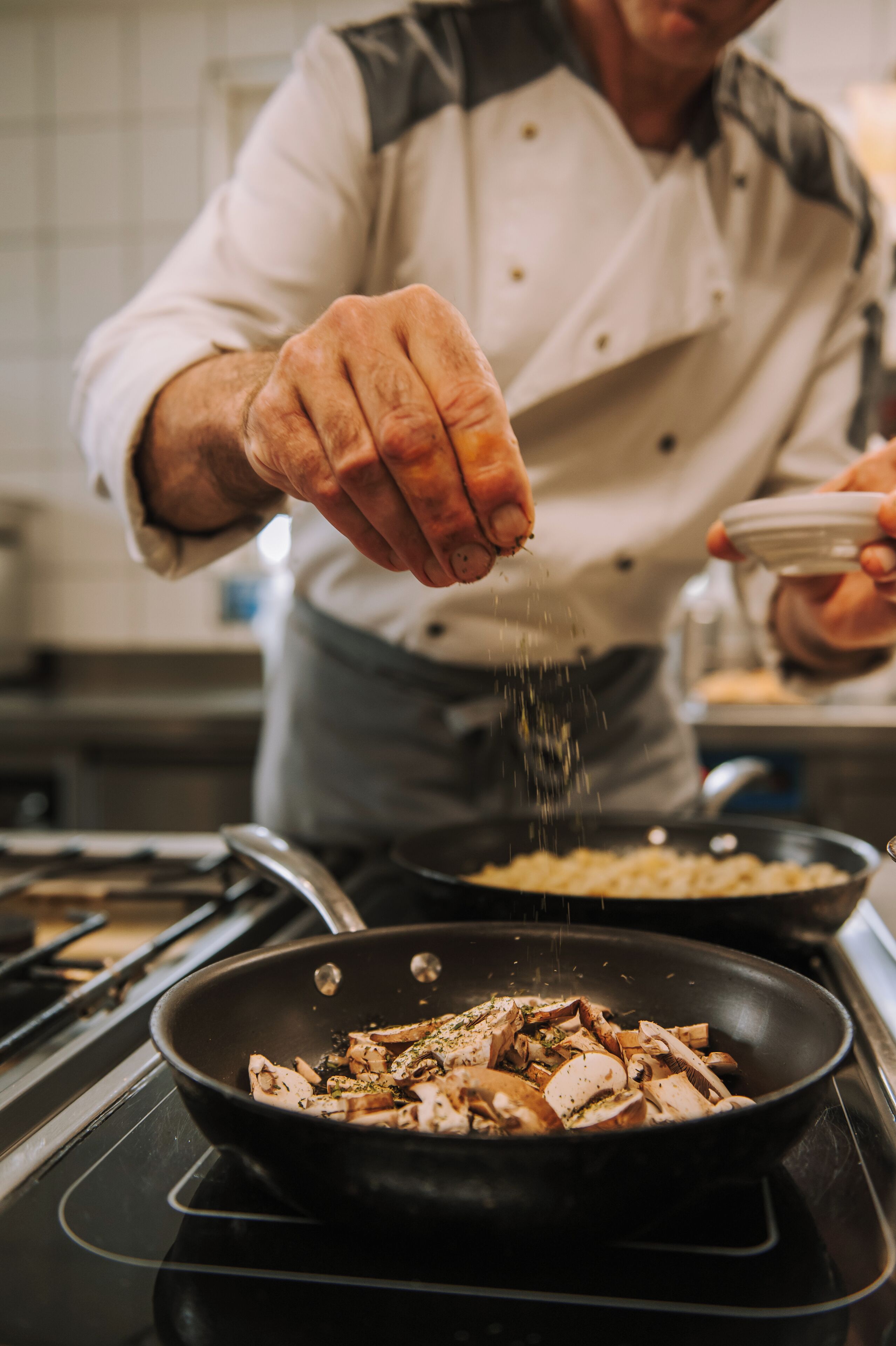 Um cozinheiro temperando comida em uma frigideira.