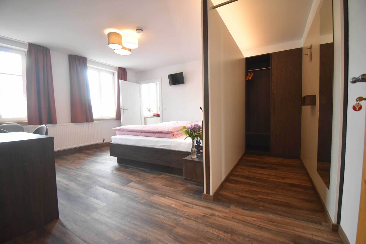Une chambre à coucher avec un lit, un bureau, une chaise, une armoire et un téléviseur fixé au mur.