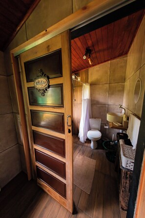 A wooden door with a nameplate, a wooden floor, a toilet, a sink, and a mirror in a bathroom. - Rancho Vô João - Space for Incredible Moments (Doutor Pedrinho)