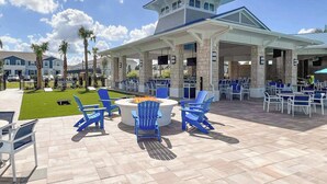 An outdoor patio area with blue chairs and a fire pit, surrounded by stone pillars and a covered seating area.
