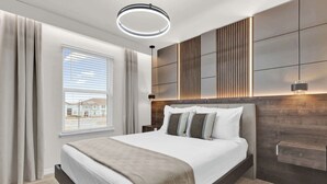 A modern bedroom with a large bed, a window with blinds, a wall-mounted light, and a wooden accent wall.