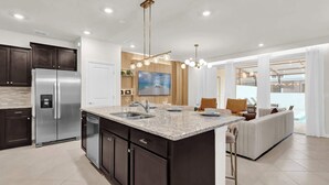 A modern kitchen with dark cabinets, a stainless steel refrigerator, and a marble countertop.