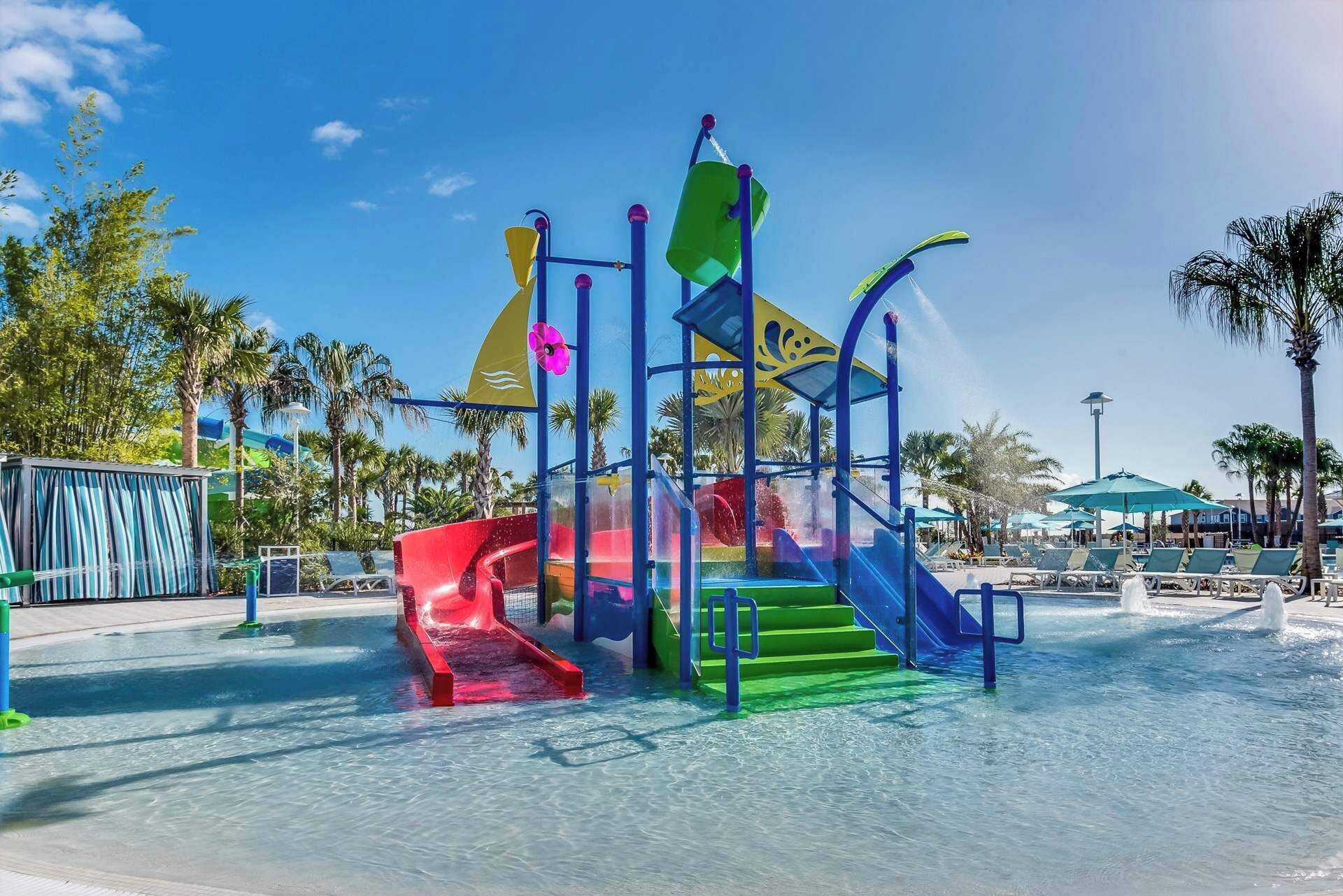 Un espace de jeux aquatiques avec des toboggans et des marches, entouré de palmiers et de parasols.