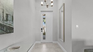 A hallway with a modern light fixture, a door leading to a balcony, and a large mirror on the wall. - Waterfront Private Pool Home With Nearby Beaches (Cape Coral)