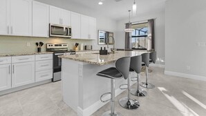 A modern kitchen with white cabinetry, a granite countertop, stainless steel appliances, and a bar area with stools. - Waterfront Private Pool Home With Nearby Beaches (Cape Coral)
