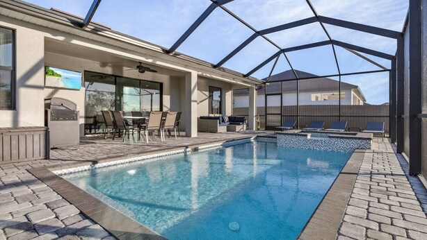 A pool area with a glass-enclosed structure, lounge chairs, and a seating area with tables and chairs. - Waterfront Private Pool Home With Nearby Beaches (Cape Coral)