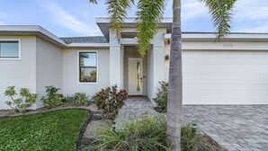 A modern two-story house with a garage, a well-maintained lawn, and various plants. - Waterfront Private Pool Home With Nearby Beaches (Cape Coral)