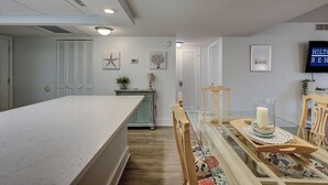 A modern kitchen with a large island, a dining area with a table and chairs, and a TV mounted on the wall. - 4205 Island Club - Folly Field - 2 Bed 2 Bath Sleeps 5 - Hilton Head Rentals (Hilton Head Island)