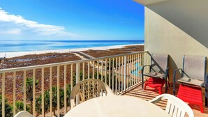 Un balcón con vista a la playa, una mesa y sillas.