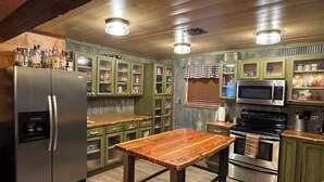 A kitchen with green cabinets, a wooden table, stainless steel appliances, and a window with blinds. - Hidden Cabin in the Woods (Pawhuska)