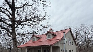 A two-story house with a red roof and a covered porch. - Hidden Cabin in the Woods (Pawhuska)