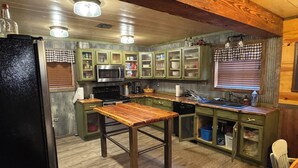 A rustic kitchen with wooden cabinets, a central island, a microwave, and a sink. - Hidden Cabin in the Woods (Pawhuska)
