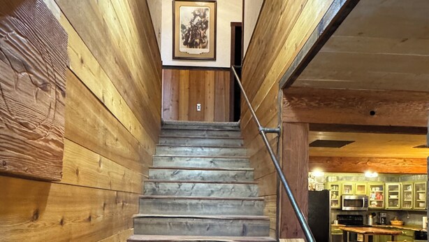 A wooden staircase leading to a lower level with a framed picture on the wall. - Hidden Cabin in the Woods (Pawhuska)