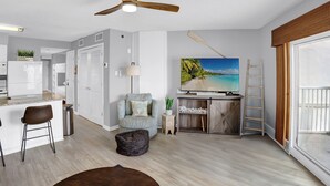 Una sala moderna con ventilador de techo, televisor, aparador de madera y vistas al exterior.