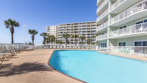 Una piscina con tumbonas y palmeras, rodeada por un hotel de varios pisos con balcones.