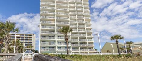 Een hoog, meerlaags hotel met balkons, een houten vogelzangpad en palmbomen.