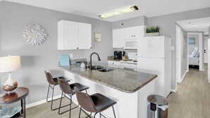 Una cocina moderna con encimera de granito, armarios blancos y una isla central con taburetes de bar.