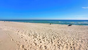 Een breed zandstrand met voetafdrukken die naar het water leiden, een helderblauwe lucht en een rustige zee.