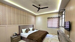 Une chambre à coucher comprenant un lit, une table de chevet, un ventilateur de plafond, un téléviseur fixé au mur et une fenêtre avec des stores.