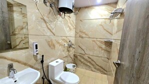 Une salle de bain avec un sol et des murs en marbre, un lavabo blanc, des toilettes et un sèche-cheveux fixé au mur.