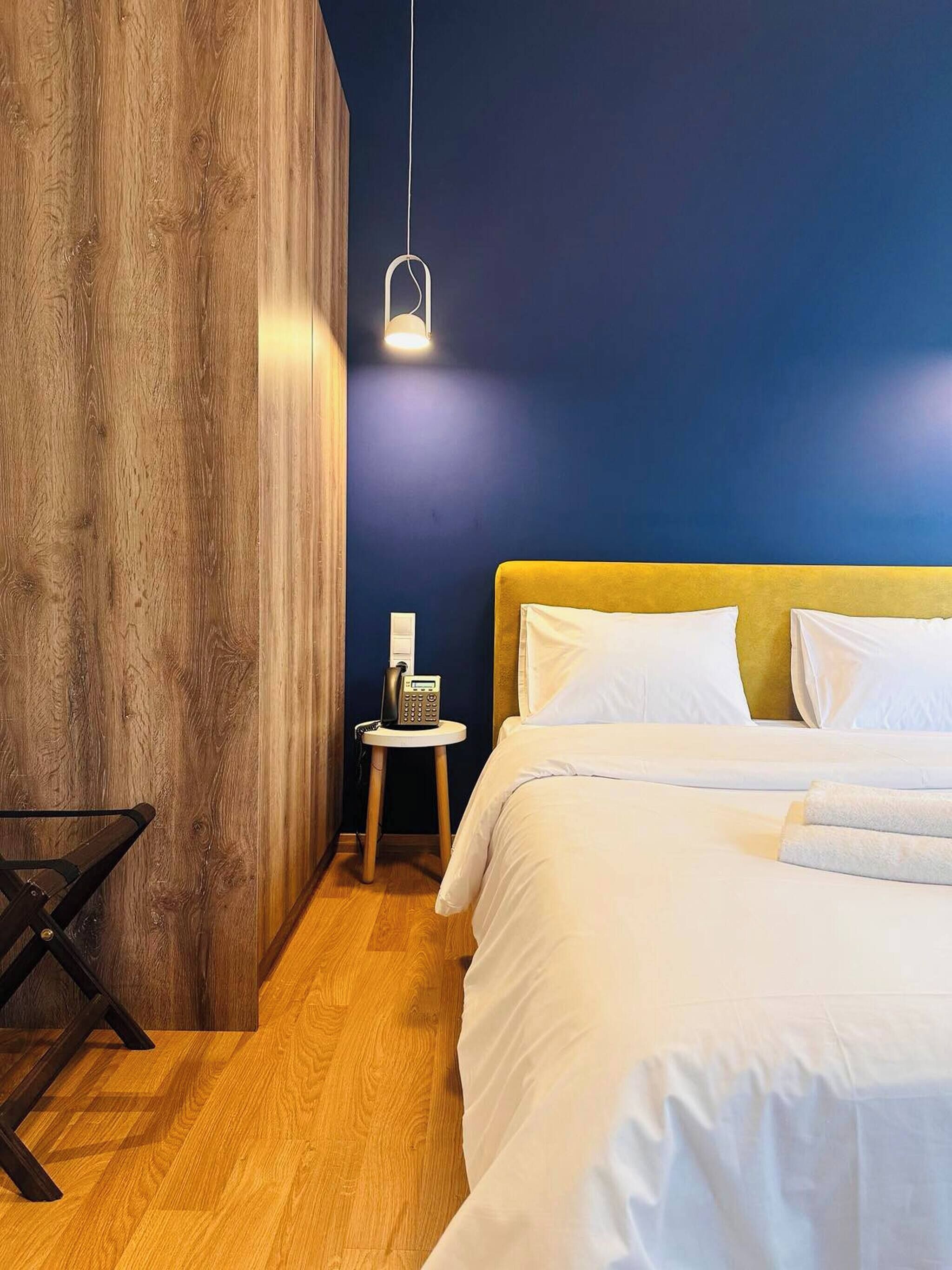 Ein Hotelzimmer mit einer Wand in Holzoptik, einem Bett mit weißer Bettwäsche, einem Nachttisch mit Telefon und einer Pendelleuchte.