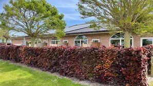 A brick building with arched windows, a solar panel roof, and a well-maintained hedge. - Apartment in Groede by the Beach (Groede)