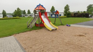 A playground with a slide and climbing structure, surrounded by grass and sand. - Apartment in Groede by the Beach (Groede)
