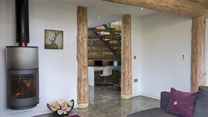 A modern living room with a wood-burning stove, a staircase leading to an upper level, and a cozy seating area. - Traditional Scandinavian/north American Log Home (Ripon)