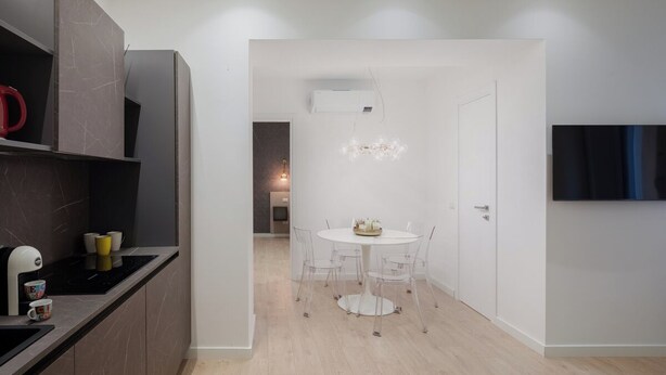 A modern kitchen with a dining area, featuring a white dining table, clear chairs, and a built-in oven.