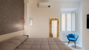 A modern bedroom with a large bed, a wall-mounted air conditioner, a decorative mirror, and a blue chair.