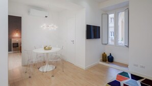 A modern dining area with a round table and chairs, a chandelier, and a television on the wall.