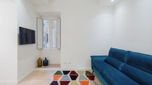 A modern living room with a blue sofa, a flat-screen TV, and a colorful geometric rug.