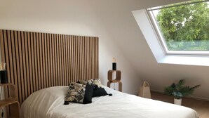 A bedroom with a slatted wooden headboard, a bed with white bedding, a bedside lamp, and a view of trees through a skylight. - Cosy, bright house close to amenities in Mordelles (Mordelles)