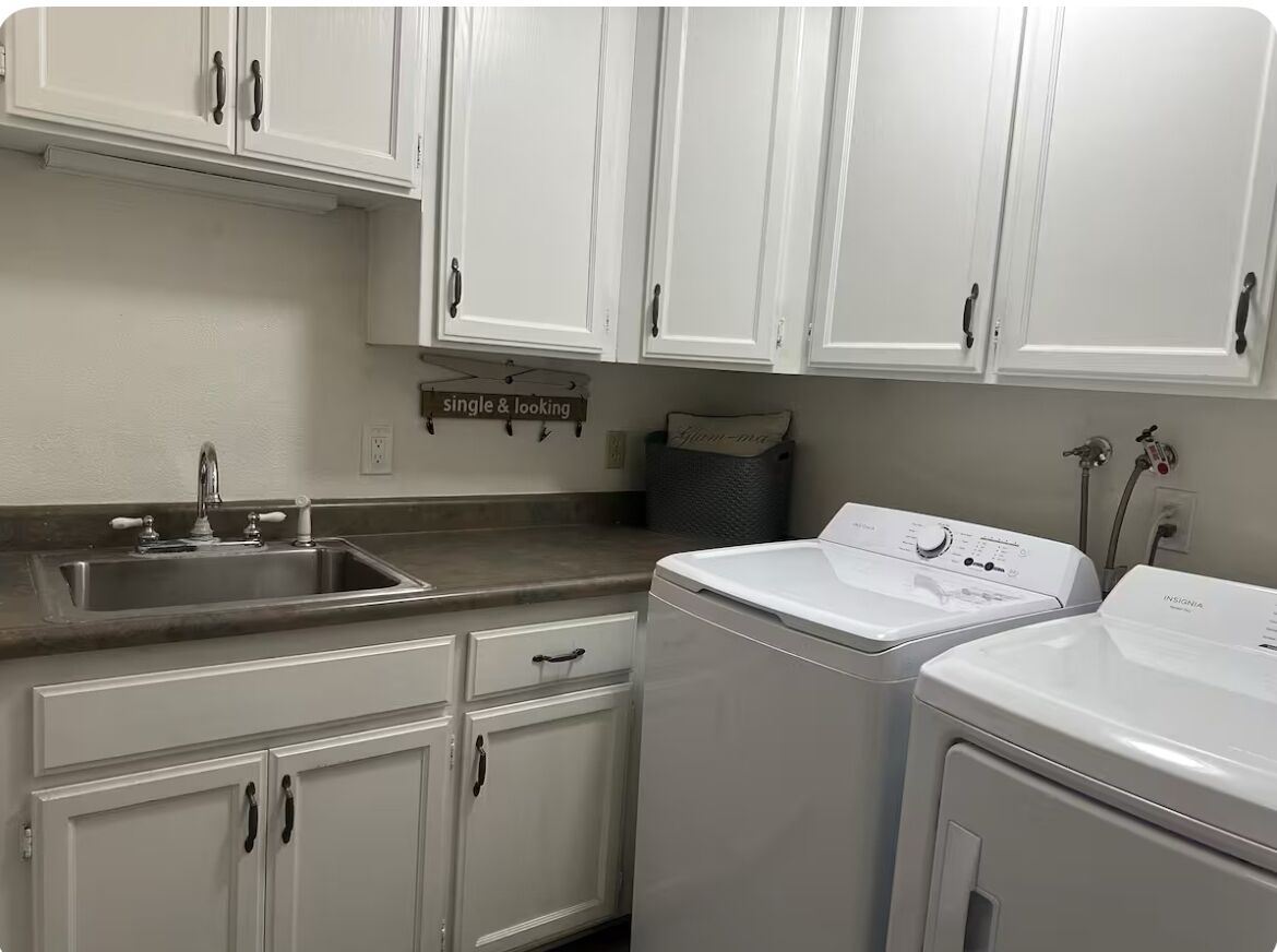 A laundry room with white cabinets, a washing machine, and a sink.