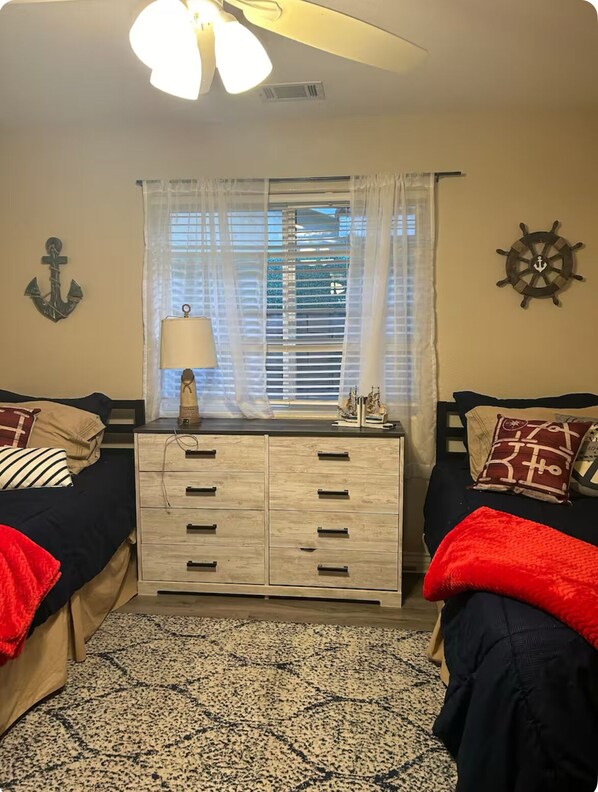 A bedroom with two beds, a dresser, a window with curtains, and nautical-themed decor. - Driftwood Cove Lake House – Waterfront, Pet-Friendly, Private Dock in Helendale (Helendale CA)