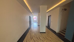 A corridor with a marble floor, white walls, and a ceiling with linear lighting. - Hotel Ishwar Palace (Danta Ramgarh)