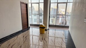 A hallway with a marble floor, a wooden door, and a yellow trash bin. - Hotel Ishwar Palace (Danta Ramgarh)