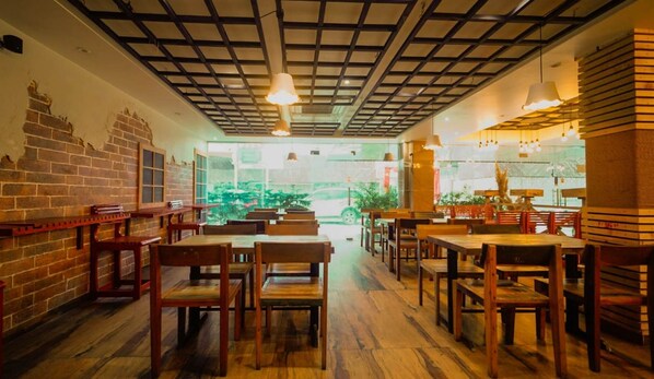 A restaurant interior with brick walls, wooden tables and chairs, and a grid-patterned ceiling. - HOTEL YUGANTAR & BANQUETS (Prayagraj)