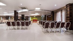 A spacious hall with rows of chairs facing a stage, a reception area with a sofa, and a decorative wall with a floral pattern.