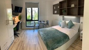 Ένα σύγχρονο υπνοδωμάτιο με κρεβάτι, γραφείο, καρέκλα και τηλεόραση.