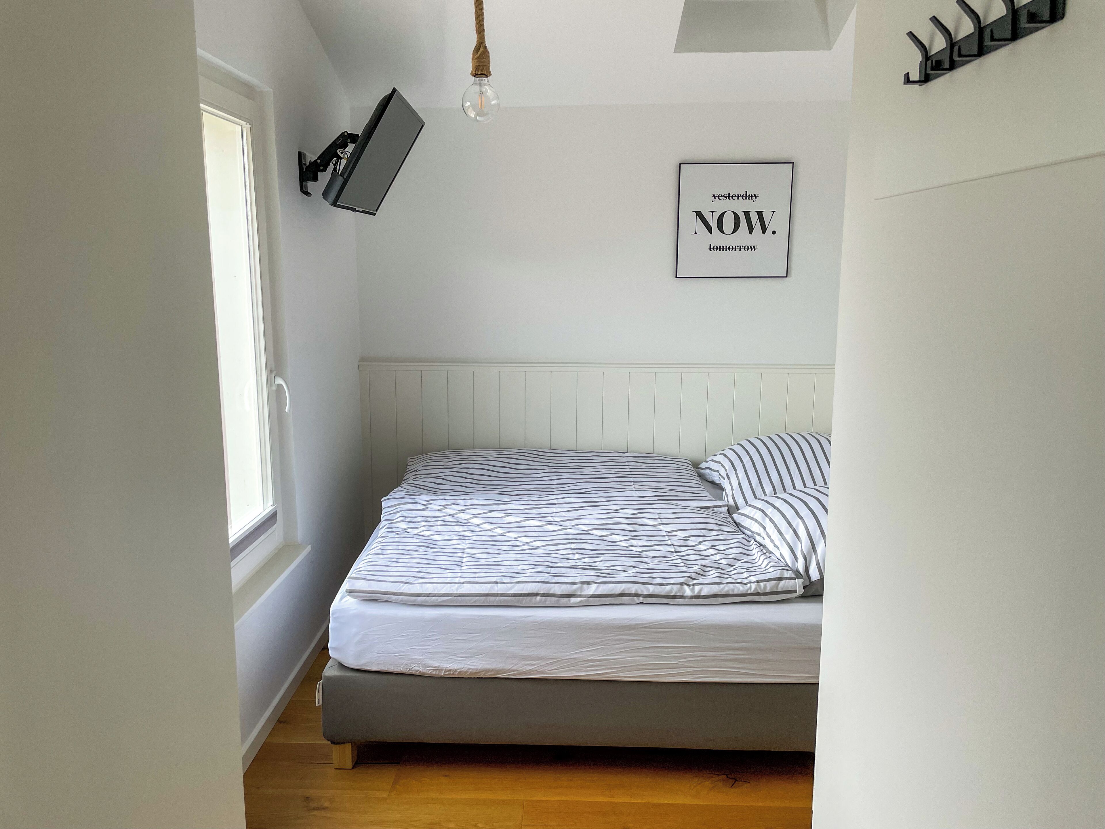 Een slaapkamer met een bed, een wandtelevisie, een gloeilamp en een motiverende quote op de muur.