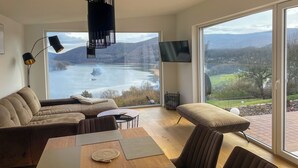 A modern living room with a large window offering a scenic view of a lake and mountains.