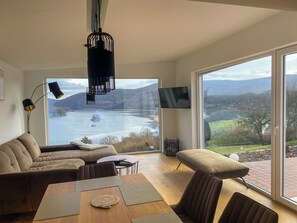 Ein modernes Wohnzimmer mit einem großen Fenster und einem herrlichen Blick auf einen See und Berge.