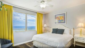 Hotellihuone, jossa on suuri sänky, yöpöytä, lamppu, tuoli ja ikkuna, jossa on verhot.