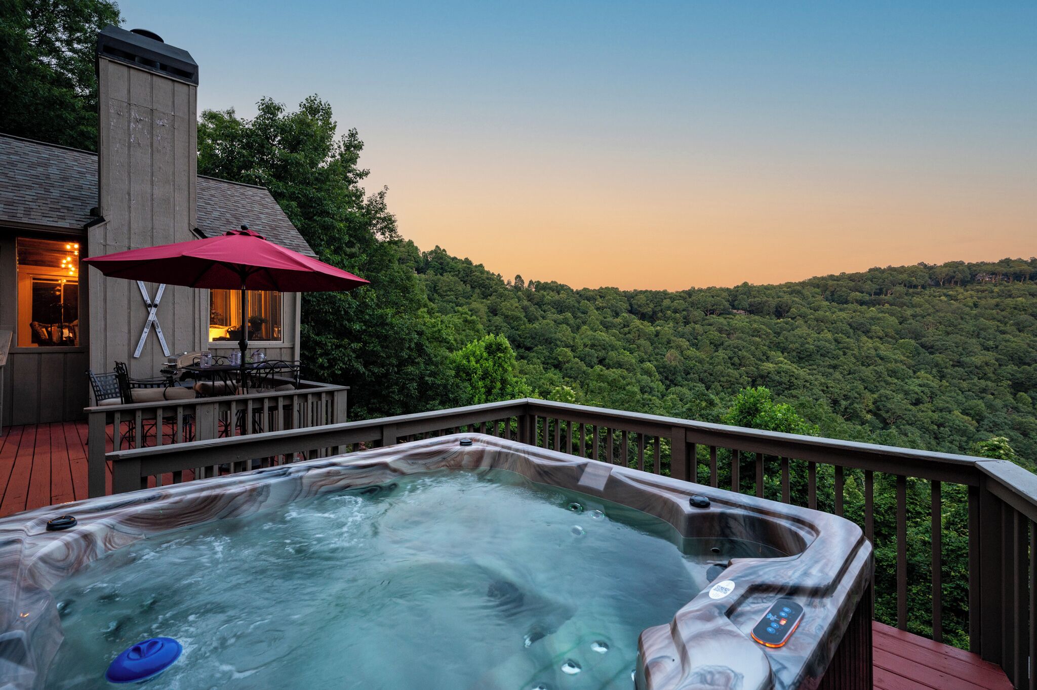 A hot tub on a deck with a view of a forested hillside.